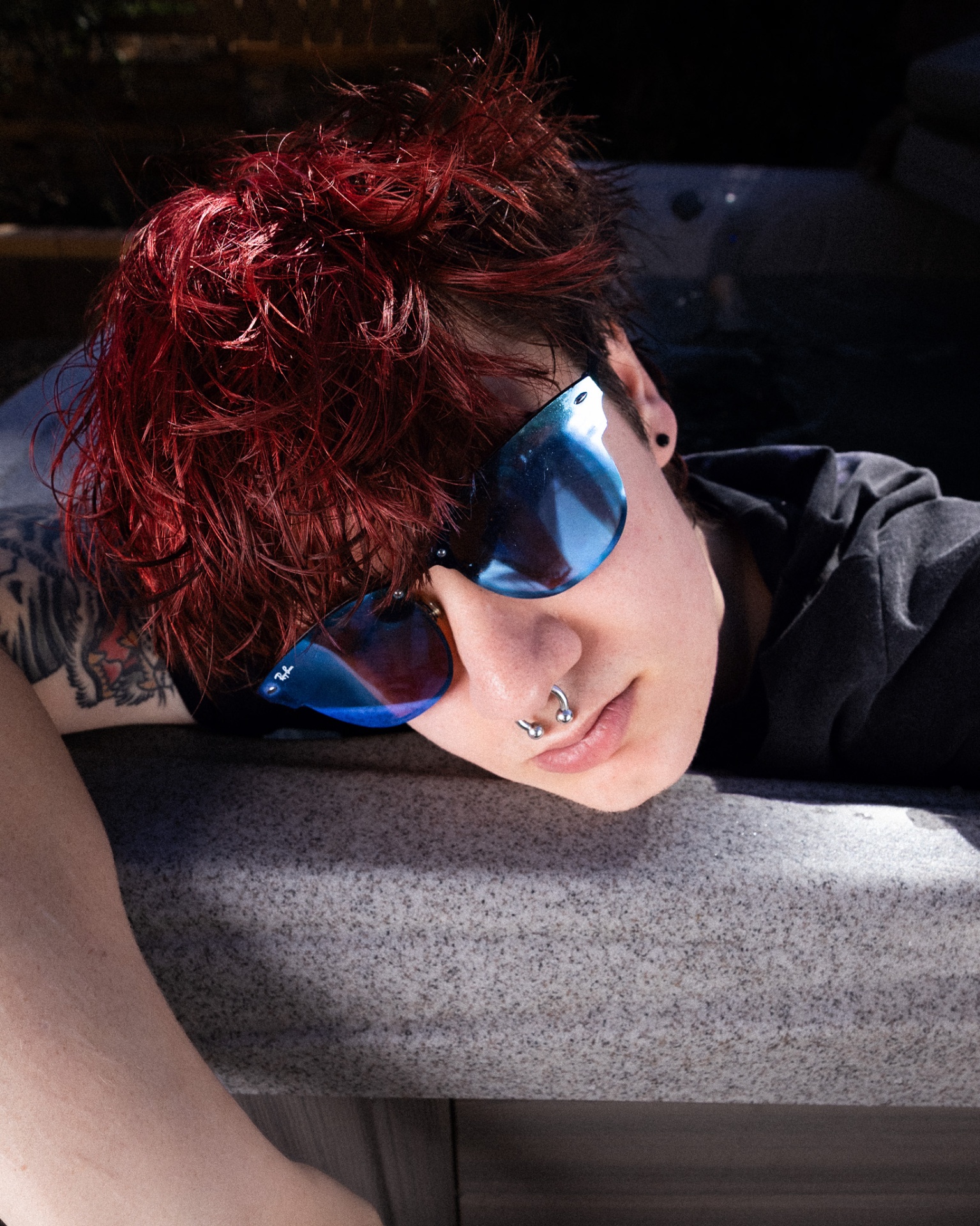 Person with red hair and blue mirrored sunglasses resting in sunlight