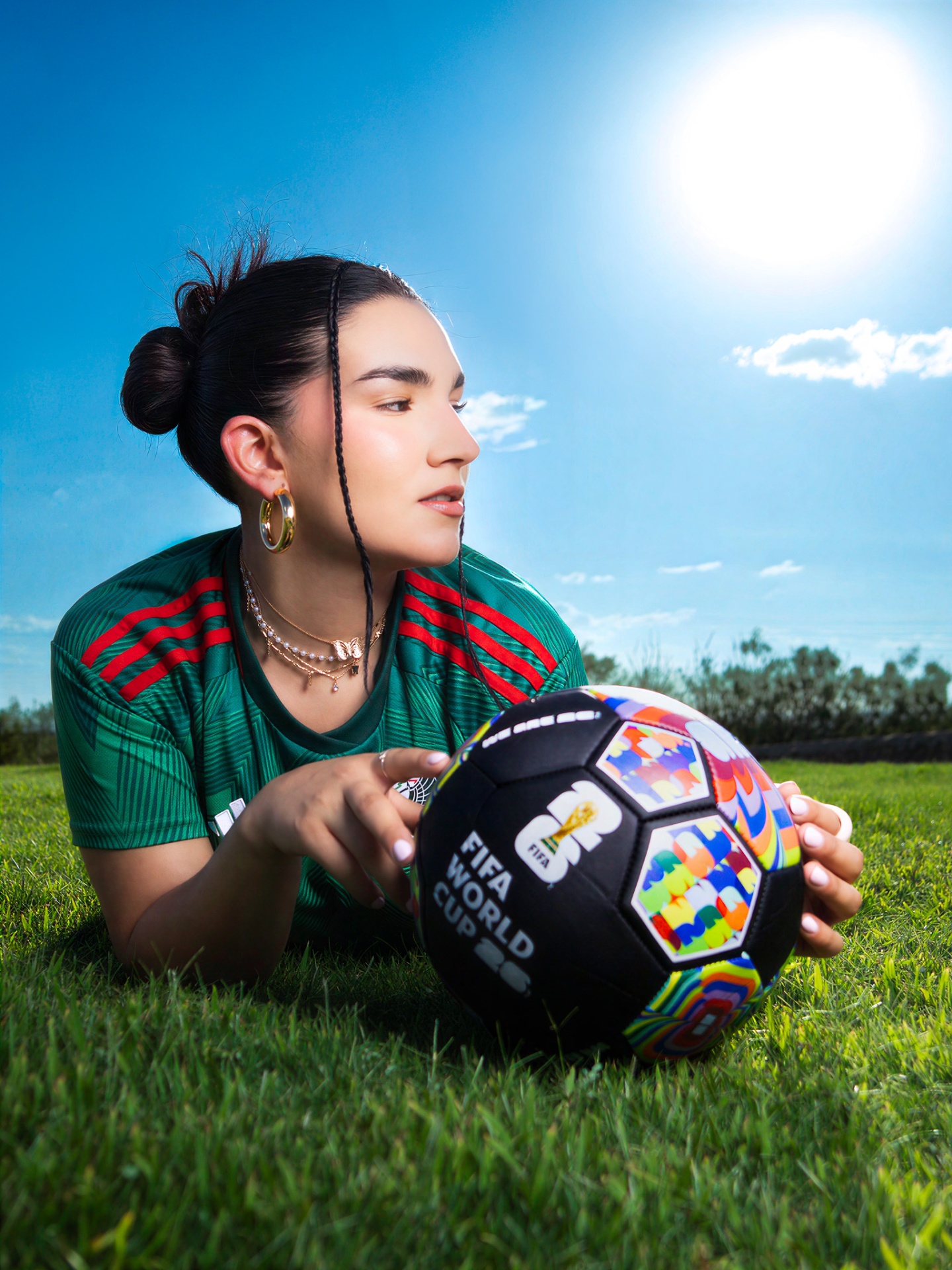 Woman in a green Mexico soccer jersey lying in grass beside a World Cup ball