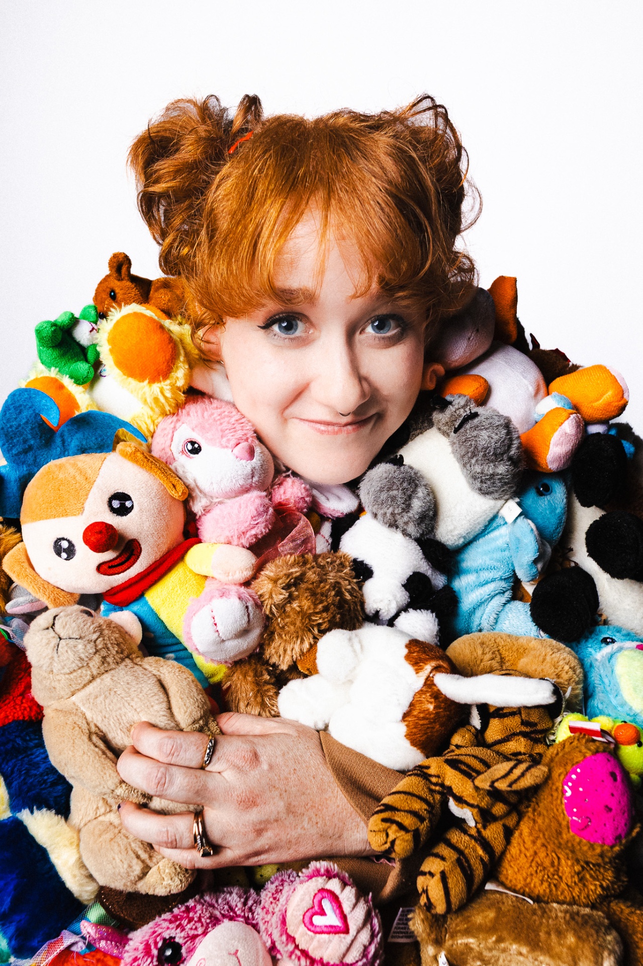 Person with red hair smiling, buried in a pile of stuffed animals