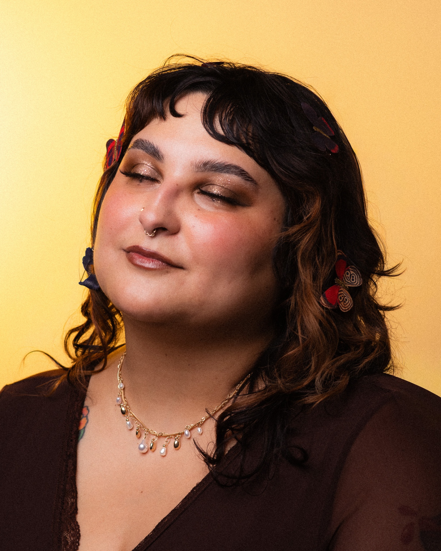 Woman with butterfly hair clips against a warm yellow backdrop, eyes closed