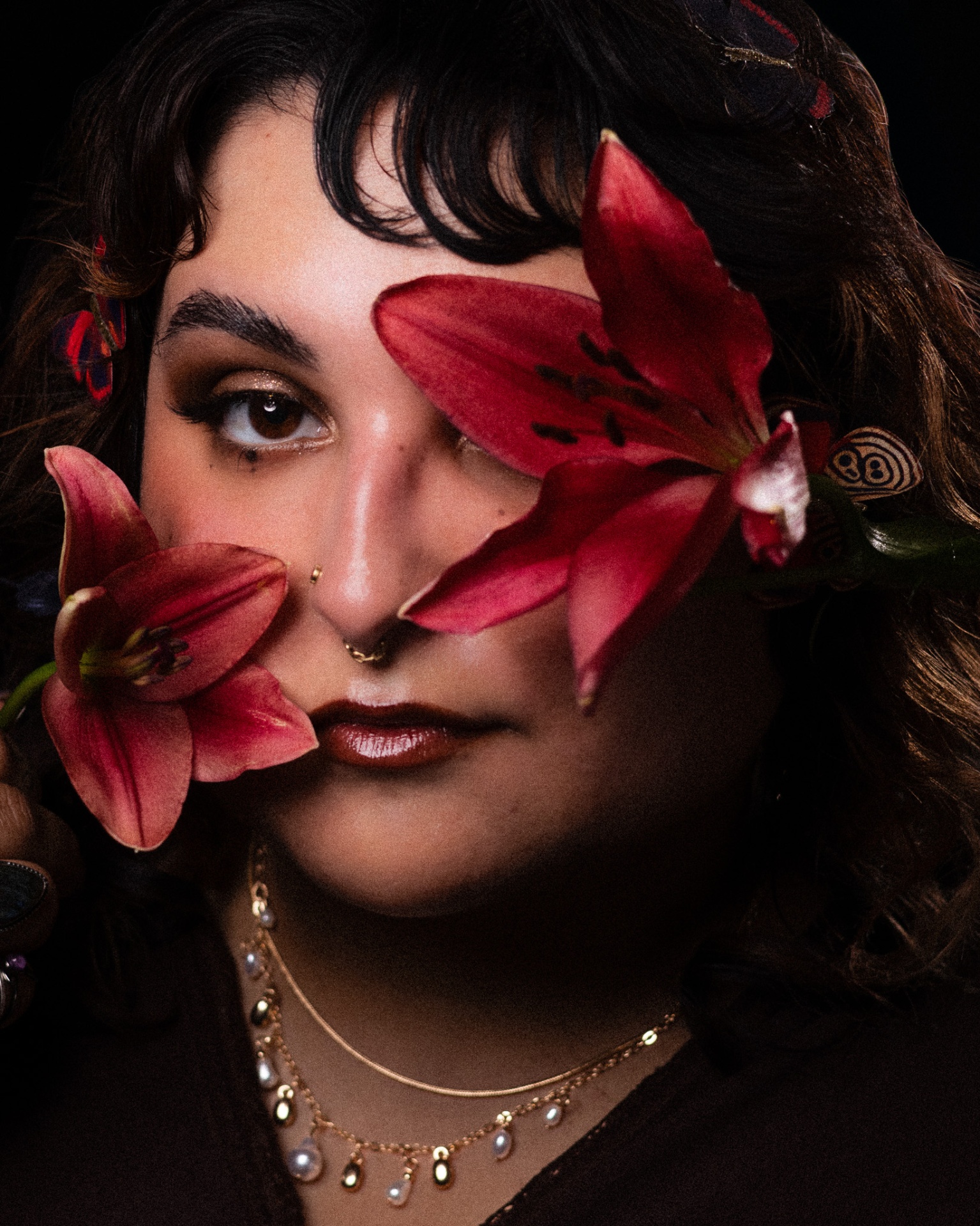Close portrait of a woman framed by red lilies in low light